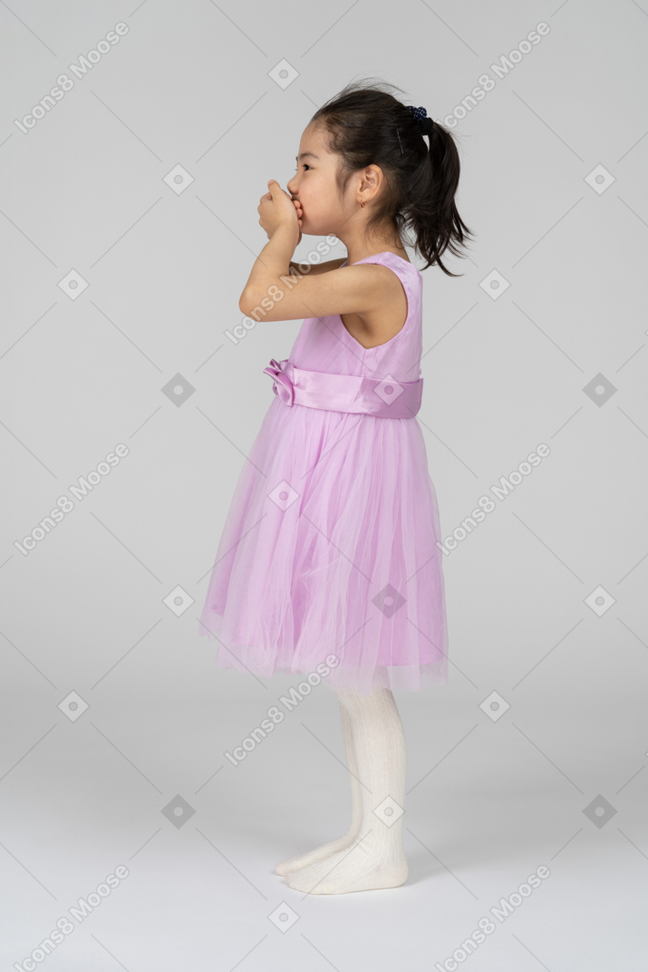 Little girl in pink dress covering mouth with her hands