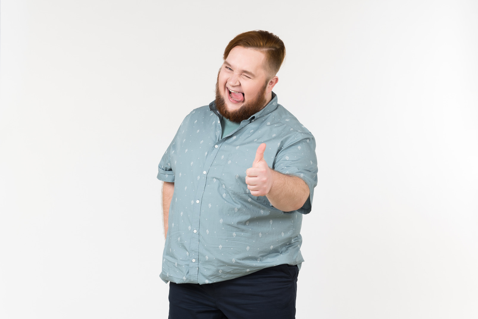 Excited young overweight man sticking tongue out and showing thumb up
