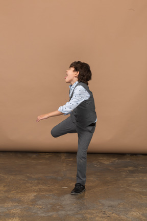 Vista lateral de um menino de terno cinza dançando
