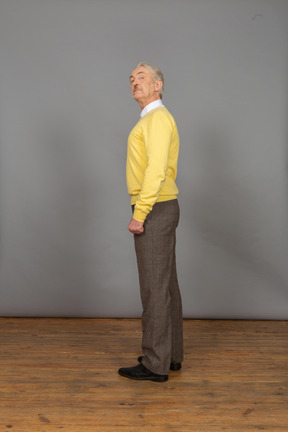 Vista lateral de un anciano curioso en jersey amarillo levantando la cabeza y mirando a la cámara