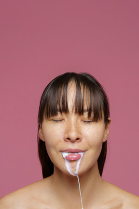 Close-up of a female standing with her eyes closed and spilling milk out of her mouth