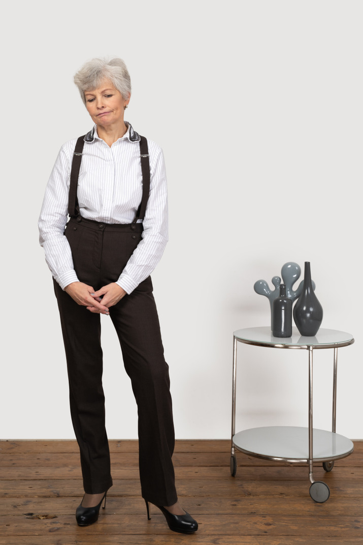 Front view of a displeased old lady in office clothing putting hands together