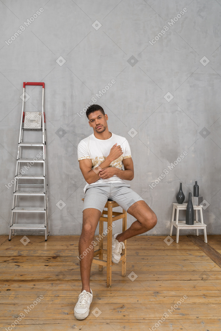 Young man sitting on stool and posing for camera
