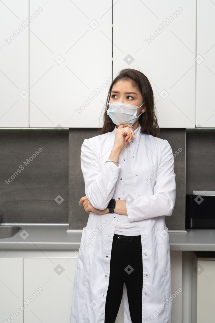 Front view of a doubtful female doctor touching chin and looking up
