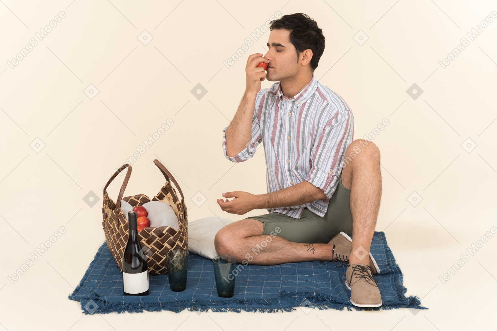 Young caucasian guy sitting on blanket and smelling fruits