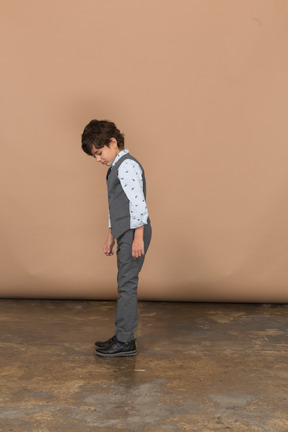 Vista lateral de un chico lindo en traje gris mirando hacia abajo