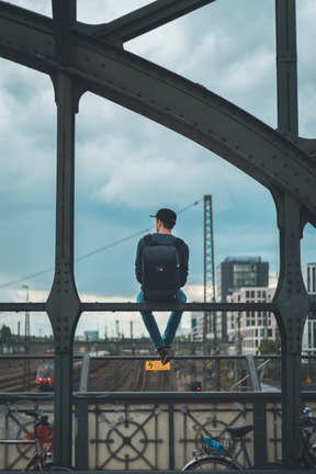 Vista traseira de um jovem sentado no corrimão da ponte