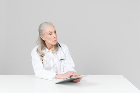 Medico femminile invecchiato che lavora su una tavoletta digitale