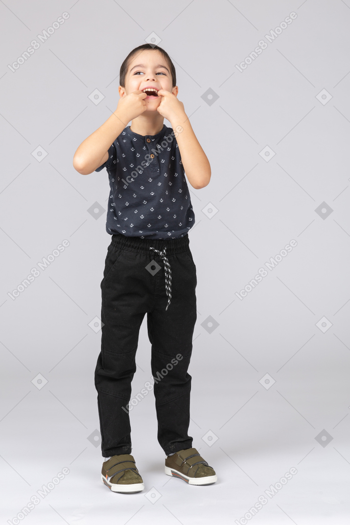 Front view of a happy boy putting fingers in mouth and looking up