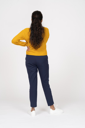 Vista posteriore di una ragazza in abiti casual in posa con la mano sull'anca