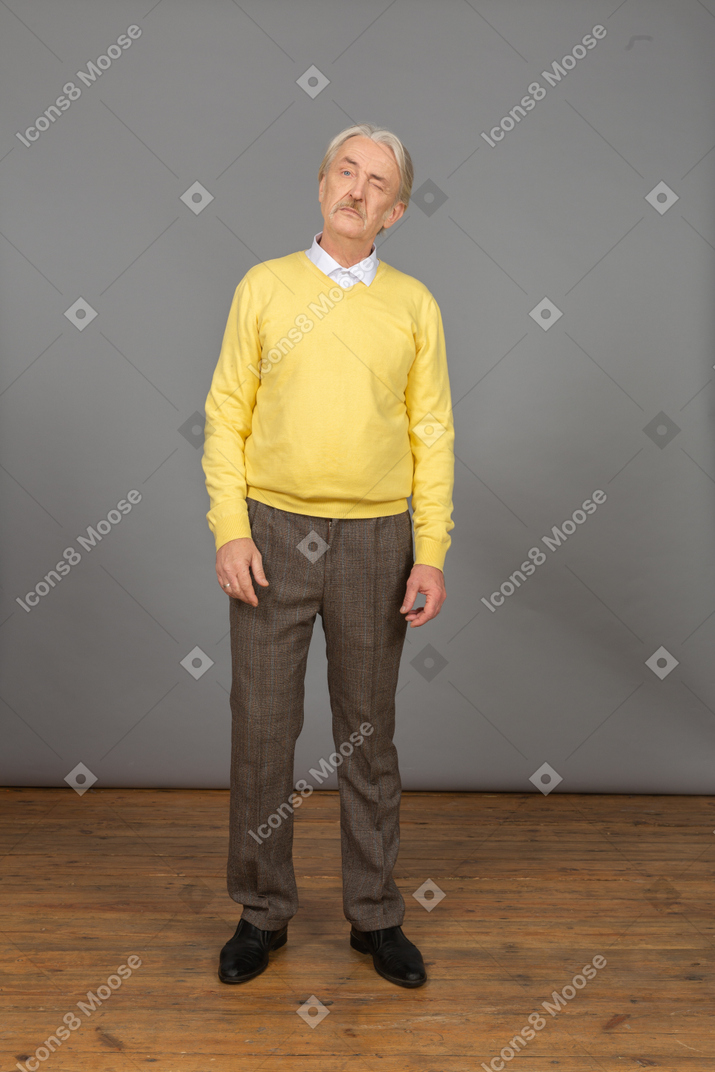 Vista frontal de un anciano curioso en jersey amarillo girando la cabeza y guiñando un ojo