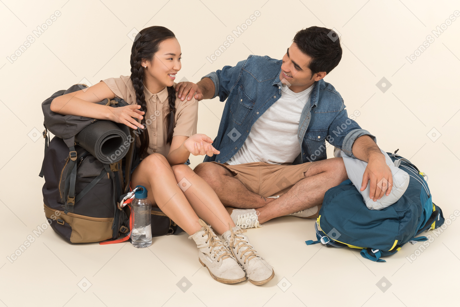 Young interracial couple sitting near backpacks and talking