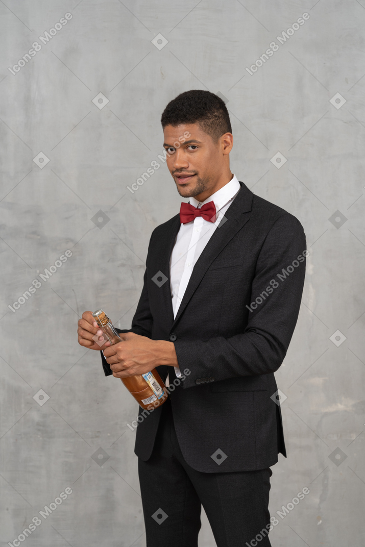 Giovane uomo in abbigliamento formale che apre una bottiglia di champagne