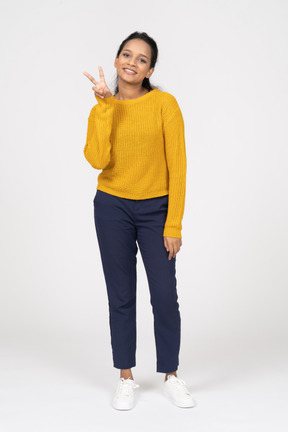 Front view of a happy girl in casual clothes showing v sign and looking at camera