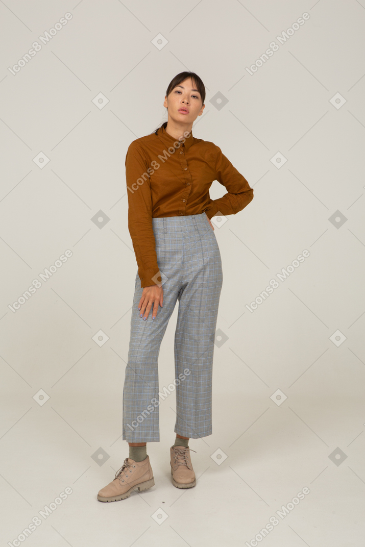 Front view of a young asian female in breeches and blouse putting hand on hi
