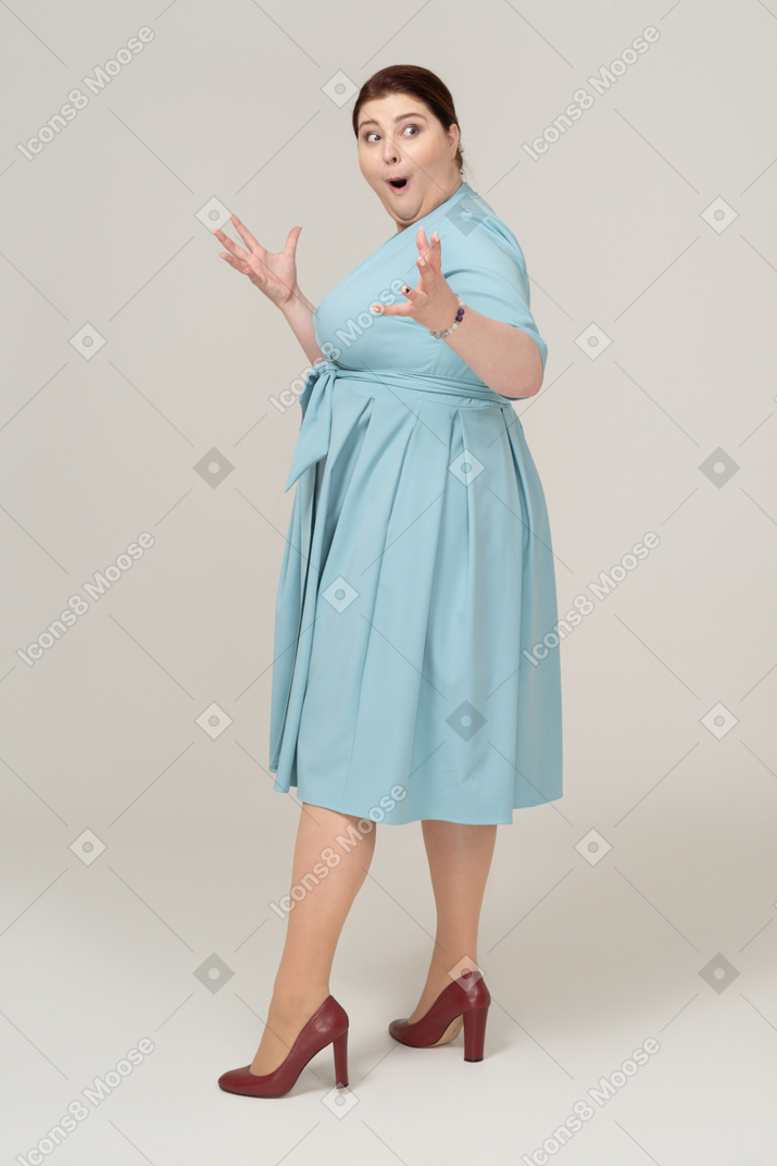 Впечатленная женщина в синем платье стоя в профиль
