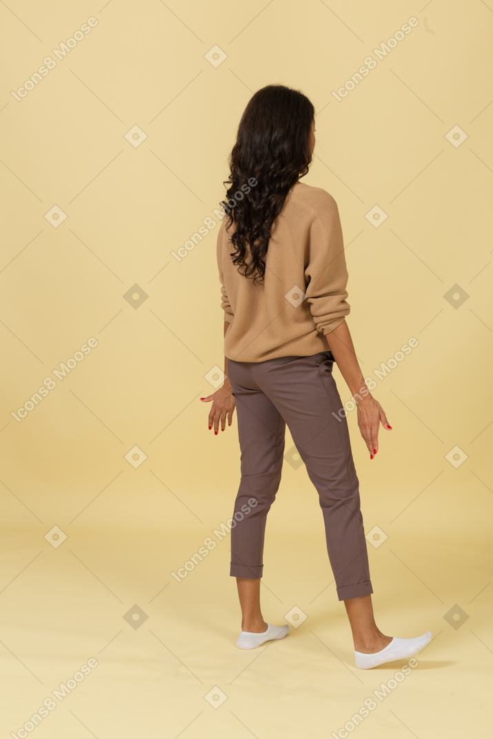 Вид сзади в трех четвертях на вопрошающую темнокожую молодую женщину, раскинувшую руки