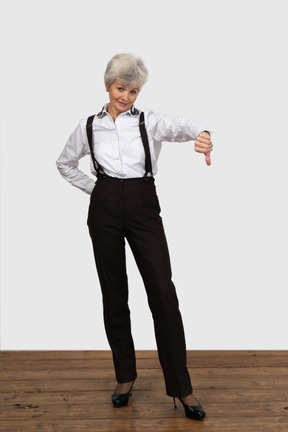 Vista frontal de una vieja mujer disgustada en ropa de oficina mostrando un pulgar hacia abajo