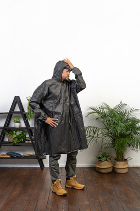 Tired man in raincoat standing with hand on hip