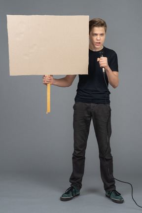 Young man speaking into a microphone and holding a poster