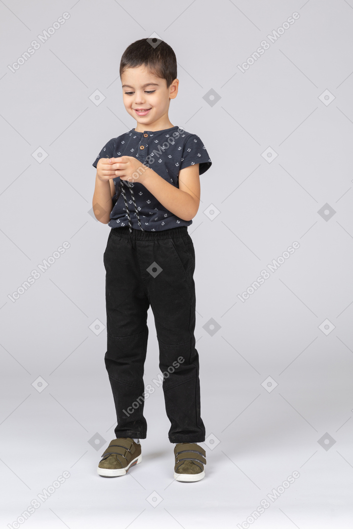 Front view of a happy boy in casual clothes looking at hands