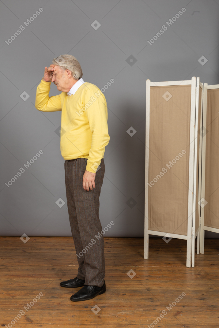 Side view of an old man having a headache while touching his forehead