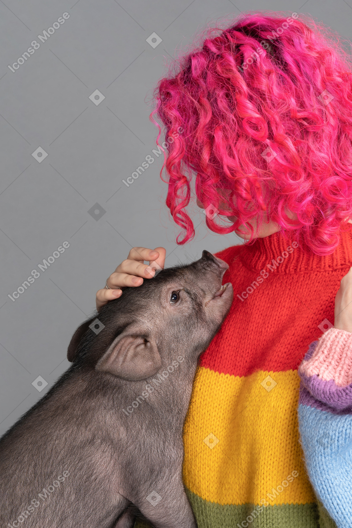 A pink haired female stroking a small pet pig