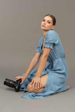 Vista lateral de uma jovem de vestido azul sentada no chão com a câmera
