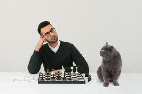 Gut aussehender mann spielt schach mit seiner katze