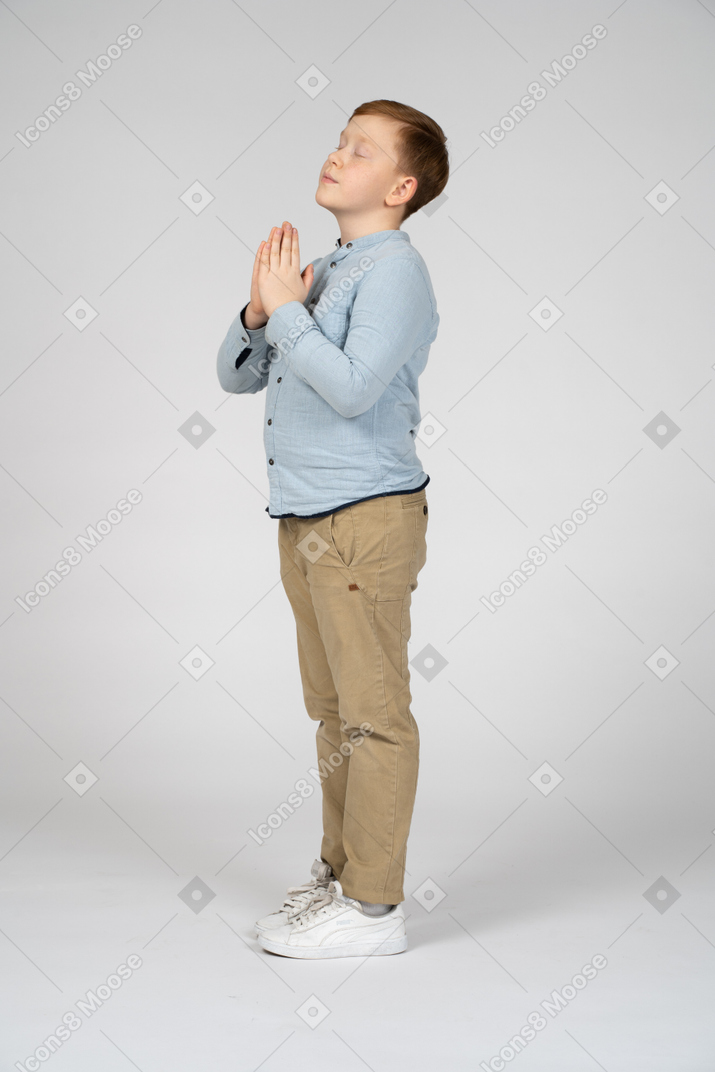 Vista laterale di un ragazzo carino che fa un gesto di preghiera