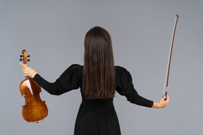 Vue arrière d'une joueuse de violon en robe noire écartant les mains