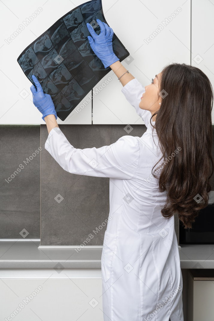 Three-quarter back view of a thoughtful female doctor analyzing x-ray image