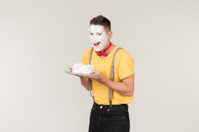 Male clown with cake cream on his face holding a cake