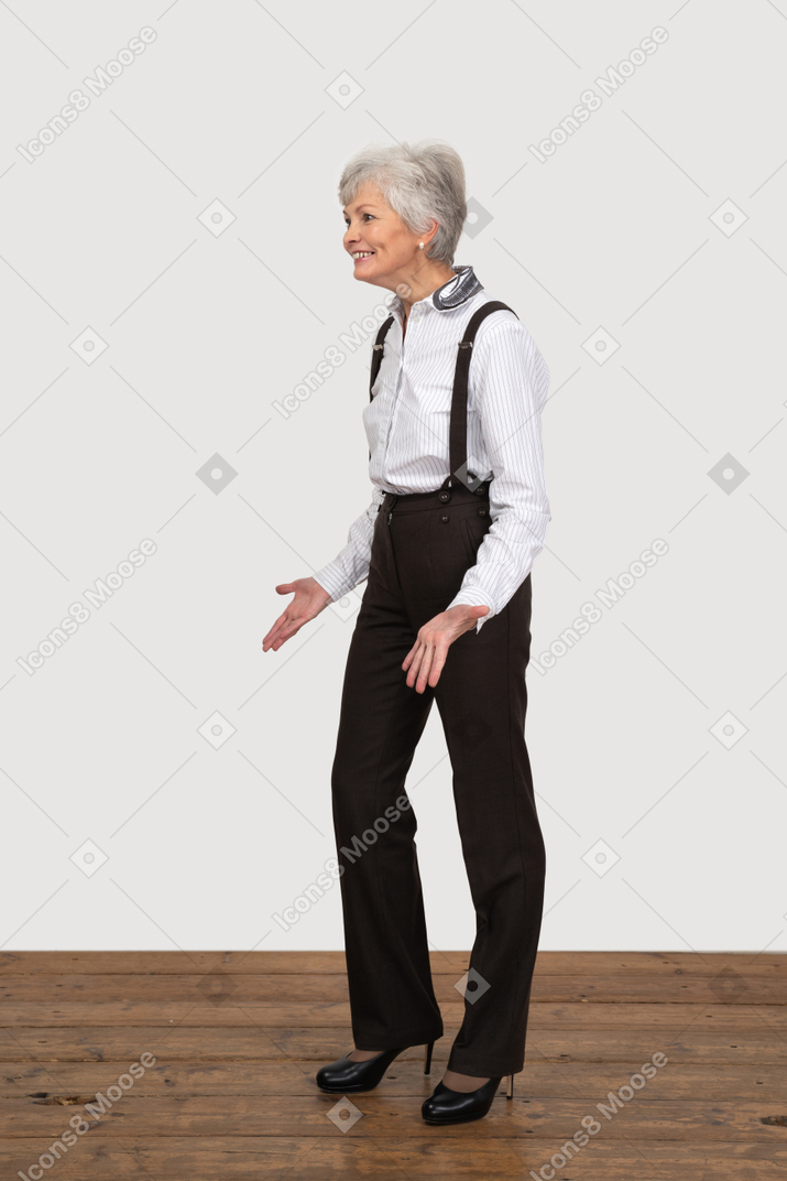 Vista di tre quarti di una vecchia signora sorridente gesticolante in abiti da ufficio