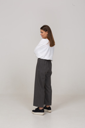 Three-quarter back view of a displeased young lady in office clothing crossing arms