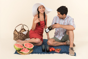 Interracial couple having picnic and guy showing bottle of wine to a girl