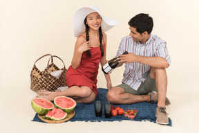 Zwischen verschiedenen rassen paare, die ein picknick haben und kerl, der einem mädchen flasche wein zeigt