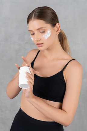 Mujer joven aplicando crema hidratante en las mejillas