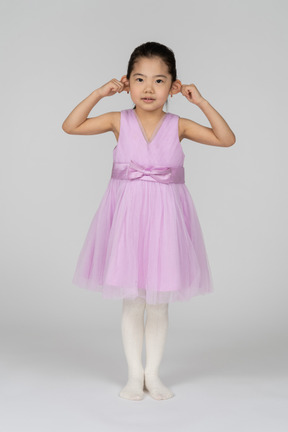 Little girl in pink dress pulling her ears