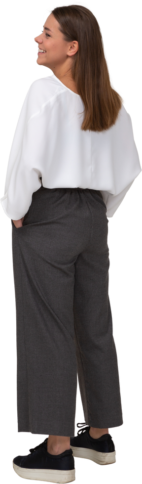 Vista posteriore di tre quarti di una giovane donna sorridente in abiti da ufficio che mette le mani in tasca