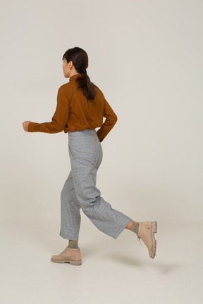 Vista posterior de tres cuartos de una joven mujer asiática corriendo en calzones y blusa