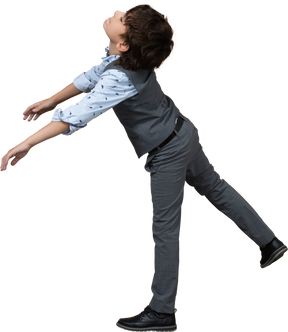 Vista lateral de un niño con traje gris parado en una pierna con los brazos extendidos