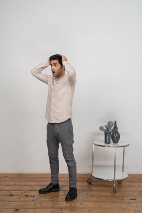 Front view of an impressed man in casual clothes standing with hands behind head