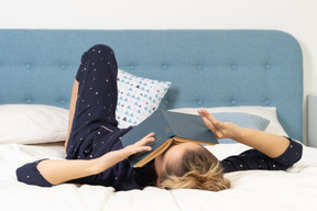 Pleine longueur d'une jeune femme ennuyée essayant de lire un livre au lit