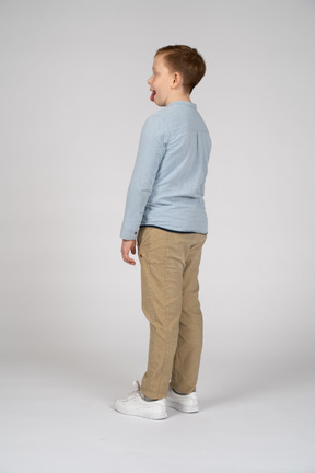 Vista laterale di un ragazzo carino in abiti casual che mostra la lingua
