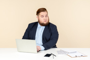 Jovem trabalhador de escritório com excesso de peso sentado na mesa do escritório e olhando por cima do ombro