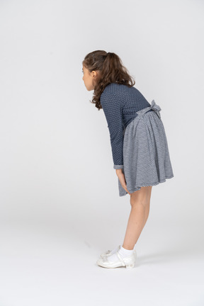 Vista trasera de tres cuartos de una niña inclinada hacia adelante y alcanzando sus rodillas