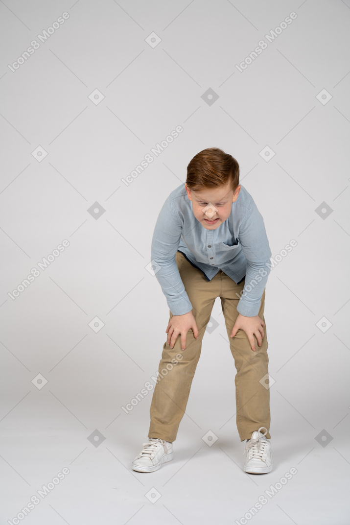Вид спереди на мальчика, наклонившегося и прикасающегося к больным коленям