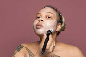 Beautiful plump afro woman applying a face cream with brush