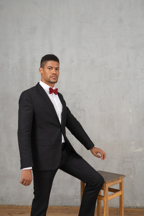 Man in black suit standing next to a stool